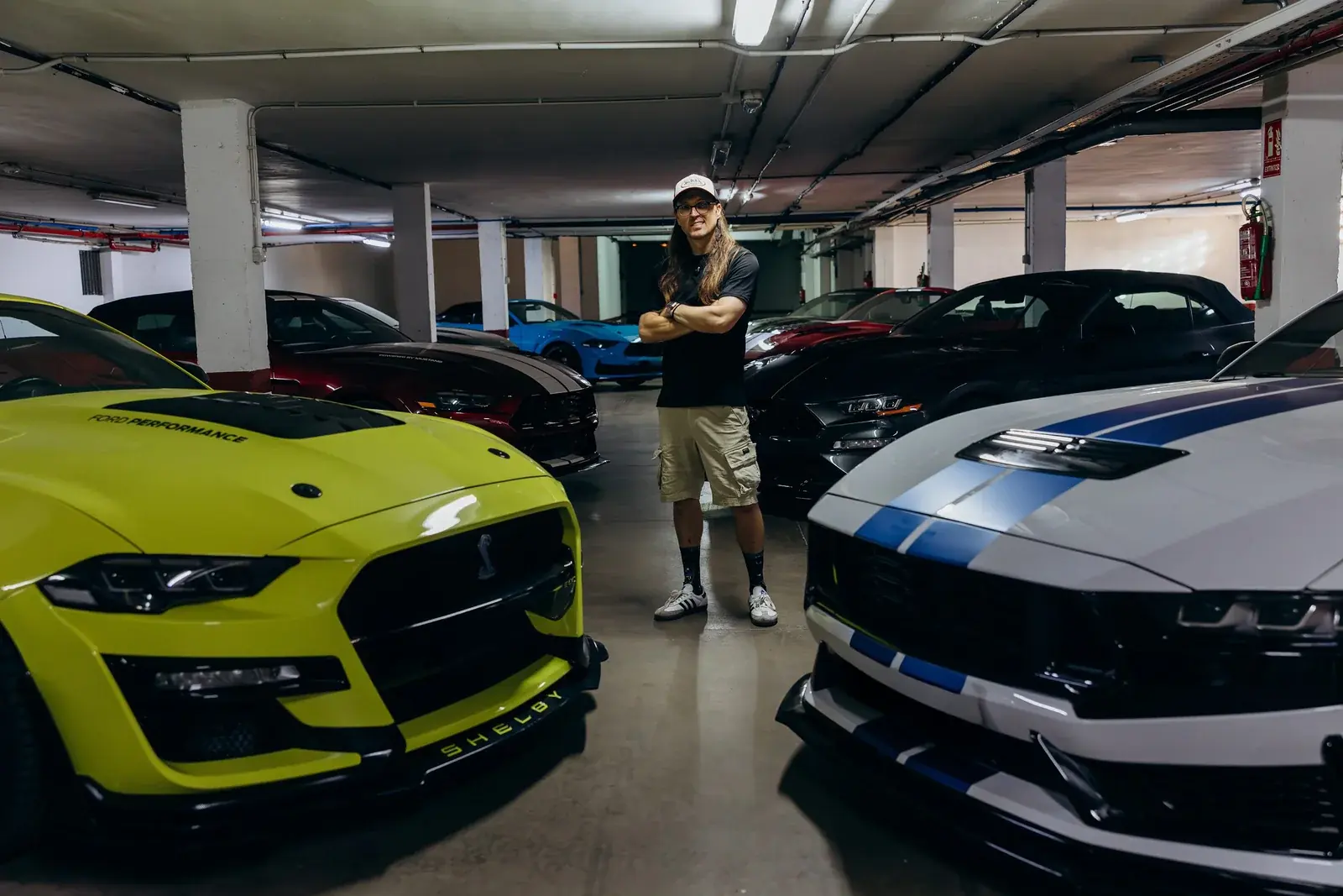 Iván Mora, arms crossed, between two Shelbys from his fleet in the garage